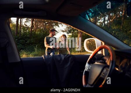 Blick vom Inneren des Autos. Lenkrad, Außenspiegel. Schöne junge Paare haben eine gute Zeit im Wald bei Tag Stockfoto
