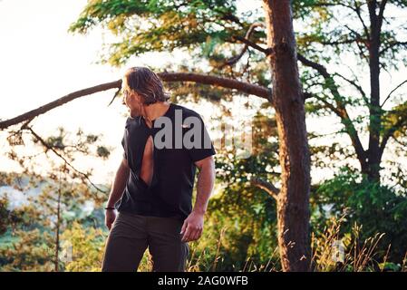 Schaut hinter. Stattlicher Mann mit muskulösen Körperbau ist im Wald bei Tag Stockfoto