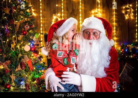 Kleines Mädchen Flüstern in Santa's Ohr. Erzählt ein Geheimnis. Das Geschenk, das Sie gerne zu gewinnen. Sprechen darüber, wie Sie während des Jahres verhalten. Stockfoto