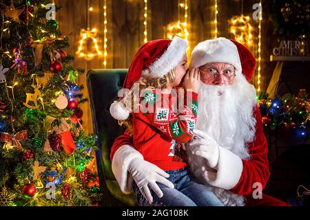 Kleines Mädchen Flüstern in Santa's Ohr. Erzählt ein Geheimnis. Das Geschenk, das Sie gerne zu gewinnen. Sprechen darüber, wie Sie während des Jahres verhalten. Stockfoto