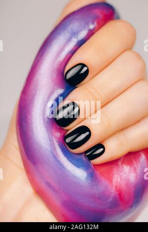 Hände mit schwarzen Maniküre holding Schleim in Blau und Rosa leuchtende Farben Stockfoto