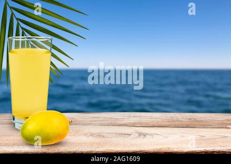 Mango und Mango Saft stehen auf dem Tisch gegen das Meer. Stockfoto