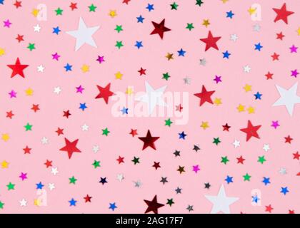 Weihnachtsdekoration bunte Konfetti Sterne gegen rosa Hintergrund Stockfoto