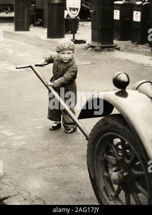 Im frühen 20. Jahrhundert vintage Pressefoto - kleines Kind in Overalls ein Auto aufbocken Stockfoto