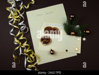 Liebes Christkind Brief geschrieben für Weihnachten. Papier und Umschlag mit Zweig der Fichte und getrockneten Schicht von Orange auf braune Oberfläche. Stockfoto