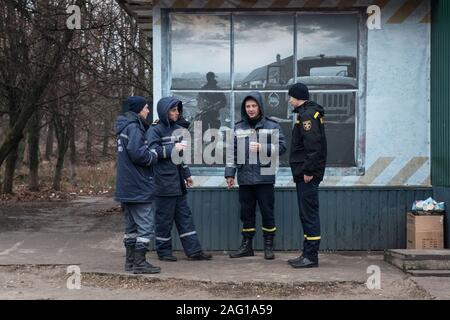 Mitarbeiter des Kernkraftwerks Tschernobyl in einer Kaffeepause während Ihrer täglichen Schicht vor einer Bar in Tschernobyl Stadt. Im Hintergrund ist ein Wandgemälde, ein liquidator in der Zone nach der Reaktorkatastrophe im April 1986 gesehen. Tschernobyl (Stadt), Tschernobyl Sperrzone, Ivankiv Rajon, Kiev Oblast, Ukraine, Osteuropa Stockfoto