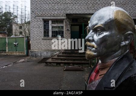 Büste von Wladimir Iljitsch Lenin am Eingang in den Bereich der Duga-1 (auch als ANDR-1 oder Russischen Specht) in der Nähe von Tschernobyl innerhalb der Sperrzone von Tschernobyl. Im Hintergrund ist der Duga-1-Array gesehen. Der E8288 ist eine Sowjetische gebaut, über dem Horizont Radar für interkontinentale ballistische Rakete startet. Die Bauarbeiten begannen im März 1972. Die ersten Sendungen aus diesem Betrieb wurden auf den 4. Juli 1976 lesen. Am Morgen des 26. April 1986 die Operationen der Radar gestoppt. Sperrzone von Tschernobyl, Invankiv Rajon, Oblast Kiew, Ukraine, Osteuropa Stockfoto