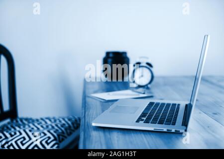 Komfortables Arbeiten im Home Office mit Holztisch und modernen Laptop auflegen. Freiberufliche Arbeit Konzept. Farbe des Jahres 2020 Classic blau Stockfoto