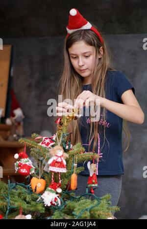 Ein junges Mädchen ziert eine kleine, natürliche Weihnachtsbaum zu Hause Stockfoto