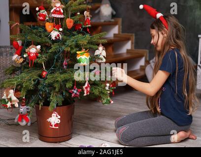 Ein junges Mädchen ziert eine kleine, natürliche Weihnachtsbaum zu Hause Stockfoto