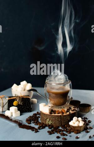 Becher Kaffee mit Dampf. Zucker und eine Handvoll Kaffee baens. Weihnachtsschmuck. blau und schwarz hintergrund Stockfoto