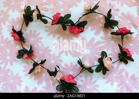 Eine Zeichenkette von Stoff Rosen in der Form eines Herzens auf eine rosa Blume Hintergrund Stockfoto