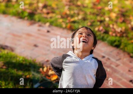 Ein kleiner Junge lachen und Glück als er blickt hinauf in den Himmel, während im vorderen Hof während der Herbstsaison. Stockfoto