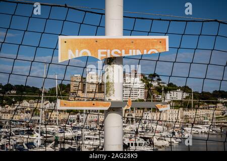 Torquay, Torbay, England, Großbritannien - Juni 04, 2019: ein beschädigtes Schild, kein Angeln, mit dem Torquay Marina, von Princess Pier gesehen, im Hintergrund Stockfoto