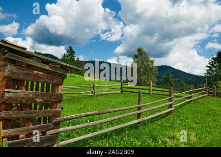 Holzzaun auf einer Ranch closeup, schönen Sommer Landschaft, Tannen auf Hügeln, bewölkter Himmel und Wildblumen - Reiseziel Scenic, Karpaten moun Stockfoto