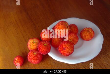 Irische Erdbeeren (Arbutus unedo) auf einem Teller auf einen hölzernen Tisch serviert. Stockfoto