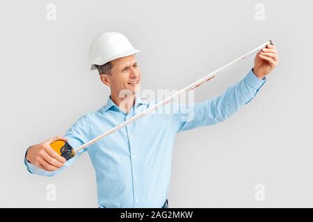 Konstruktion. Reifer Mann in hardhat Ständigen isoliert auf Weiss mit Magnetband Maßnahme Stockfoto