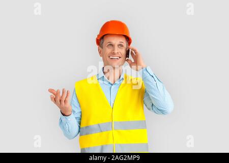 Konstruktion. Reifer Mann in hardhat und einheitlichen ständigen isoliert auf Weiss im Gespräch mit Freund auf dem Smartphone freudige Stockfoto