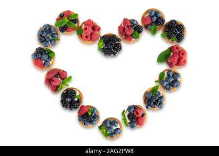 Nützliche Törtchen mit Blaubeeren, Heidelbeeren, Himbeeren in der Form eines Herzens auf weißem Hintergrund. Stockfoto