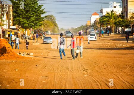Mbour SENEGAL - Apr 26, 2019: Unbekannter senegalesischen Männer sind zu Fuß eine staubige Straße mitten in der Stadt. Es gibt ein Auto auf dem Sand. Es ist Stockfoto