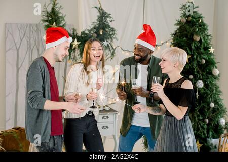 Männer froh und zufrieden, meine Damen Gläser Champagner während der Kommunikation und Lachen auf Neues Jahr Partei. Sie indische Lichter in den Händen du Stockfoto