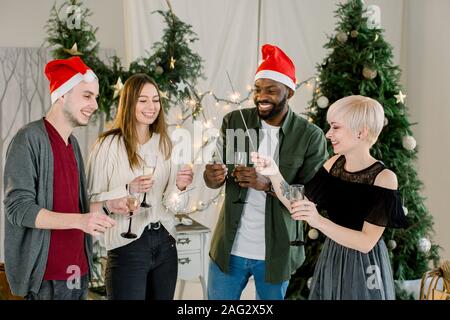 Männer froh und zufrieden, meine Damen Gläser Champagner während der Kommunikation und Lachen auf Neues Jahr Partei. Sie indische Lichter in den Händen du Stockfoto