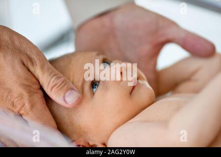 Baby Girl's Kopf durch die Hände ihres Vaters geschaukelt wird. Stockfoto