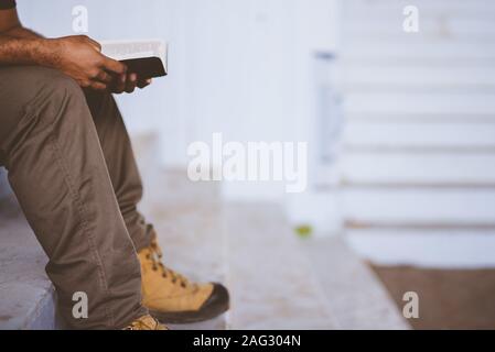 Mann sitzt auf der Treppe beim Lesen der bibel mit Ein unscharfer Hintergrund Stockfoto