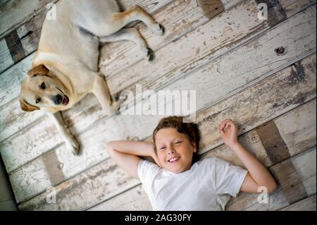 Porträt eines lächelnden Teenager liegend mit den Händen hinter seinem Kopf auf einem Parkett neben seinem Hund. Stockfoto