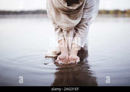 Nahaufnahme einer Frau, die eine biblische Robe im Stehen trägt Im Wasser, während sie ihre Hände wusch Stockfoto