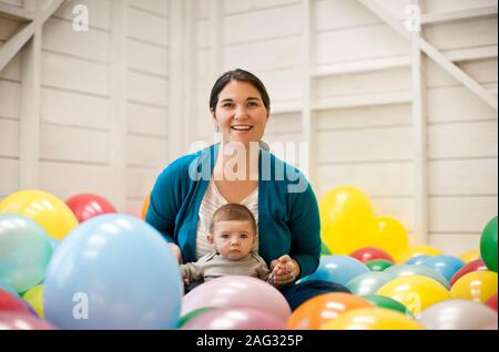 Frau und ihr Baby Sohn sitzen in einem Raum voller Luftballons. Stockfoto