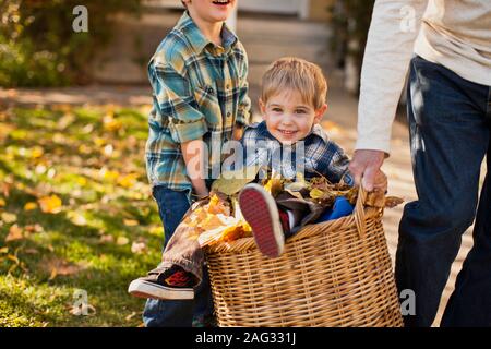 Portrait der Junge sitzt auf dem Korb und wird von seinem Bruder und Großvater durchgeführt. Stockfoto