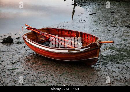 Rotes Schlauchboot auf dem Schlamm liegend mit zwei Rudern liegend Innen bei Ebbe auf einem Gezeitenfluss Byth in Suffolk Stockfoto