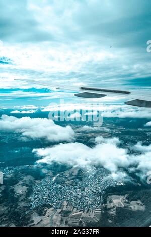 Vertikale Aufnahme eines Flugzeugflügels von innen umgeben Durch Wolken und die Stadt darunter Stockfoto