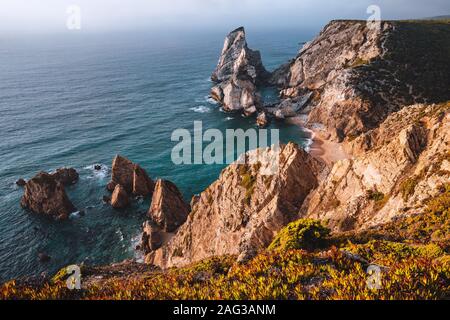 Praia da Ursa Strand mit Felsen im Vordergrund beleuchtet nach Sonnenuntergang. Surreale Landschaft von Sintra, Portugal. Atlantik Küste Landschaft Stockfoto