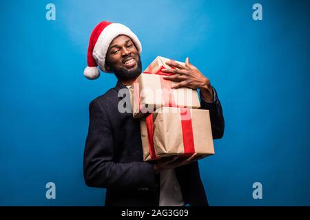 Junge afrikanische amerikanische Mann im Santa Hut Holding präsentiert auf blauem Hintergrund Stockfoto