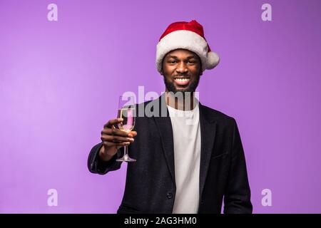 Junge afrikanische Mann in Santa hat trinken Champagner auf violette Hintergrund Stockfoto