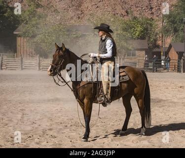 Eine Arbeitsgruppe cowgirl Wrangler auf ihr Pferd in einer staubigen auf einer Ranch in der Nähe von Moab, Utah corral. Sie trägt leder chaps aus dornige Bürste zu schützen, während Stockfoto