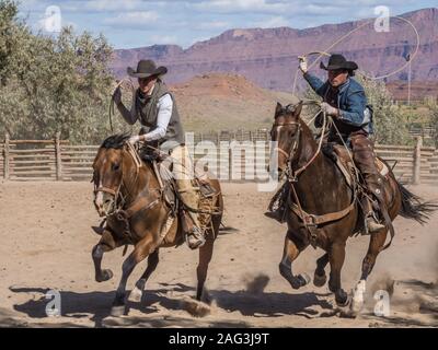 Eine Arbeitsgruppe Cowboy und Cowgirl Galopp in einer Hürde auf einer Ranch in der Nähe von Moab, Utah. Im Hintergrund sind die sandsteinfelsen der Canyon des Colorado Stockfoto