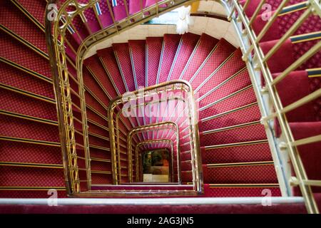 High-Winkel-Aufnahme einer rosa Wendeltreppe mit golden Griffe in einem schönen Gebäude Stockfoto