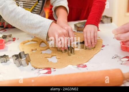 Hände von zwei Kindern helfen ihrer Mutter, traditionelle Weihnachten Ingwerkekse aus Teig zu machen und Ausschneiden Formen und Formen für das Backen Stockfoto