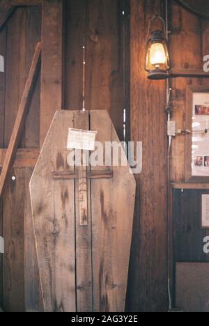 Vertikale Aufnahme eines Sarges aus Sperrholz mit einem Die Kreuzschnitzerei und die Glühbirne, die an der Tür hängt Stockfoto