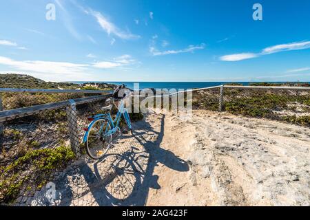 Schöne Aufnahme von einem blauen Fahrrad auf einem sandigen geparkt Straße, die zum Meer unter dem hellen Himmel führt Stockfoto