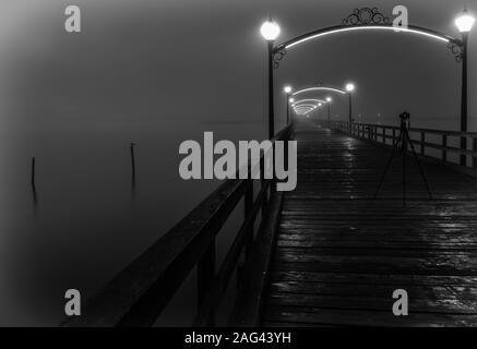 Ein Kameraständer in der Mitte einer Holzbrücke Mit beleuchteten Laternen, die in Nebel gehüllt sind Stockfoto