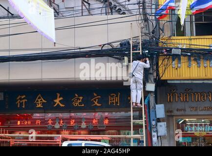 Bangkok, Thailand - Dezember 16, 2019: Closeup Arbeiter stehen auf der Leiter der Inspektion und Reparatur von kommunikationsleitungen vor Gold shop in chinat Stockfoto