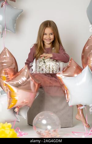 Lustige Blonde Mädchen auf einem weißen Hintergrund zu den Ballons mit einem Blumenstrauß von Wildblumen Stockfoto