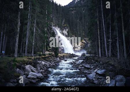 Faszinierende Low-Angle-Aufnahme eines Wasserfalls auf einem Felsen Umgeben von einem Wald von hohen Fichten Stockfoto