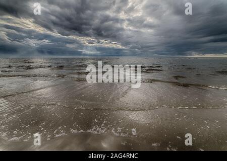 Schöne Aufnahme des sandigen Ozeans unter dem dunklen Himmel Mit der Sonne hinter den Wolken versteckt Stockfoto