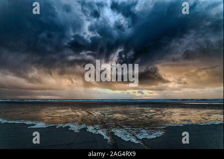 Atemberaubende Aufnahme des Ozeans vom dunklen wolkigen Himmel bedeckt Mit der Sonne hinter den Wolken versteckt Stockfoto