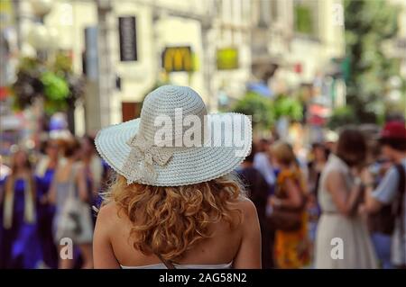 Blonde Frau mit einem weißen Hut in einem überfüllten stehen Straße auf einem unscharfen Hintergrund Stockfoto